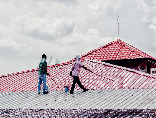 Contractors repainting metal roof as part of roof maintenance service