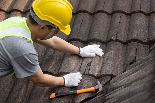 Technician repairing cracked roof tiles during roof leak inspection