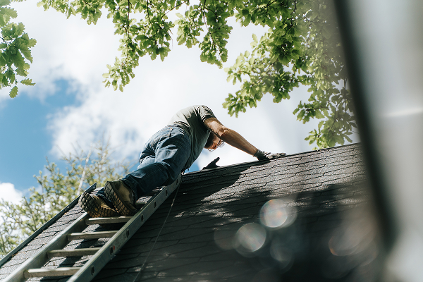 Contractor climbing ladder to inspect roof for leakage issues
