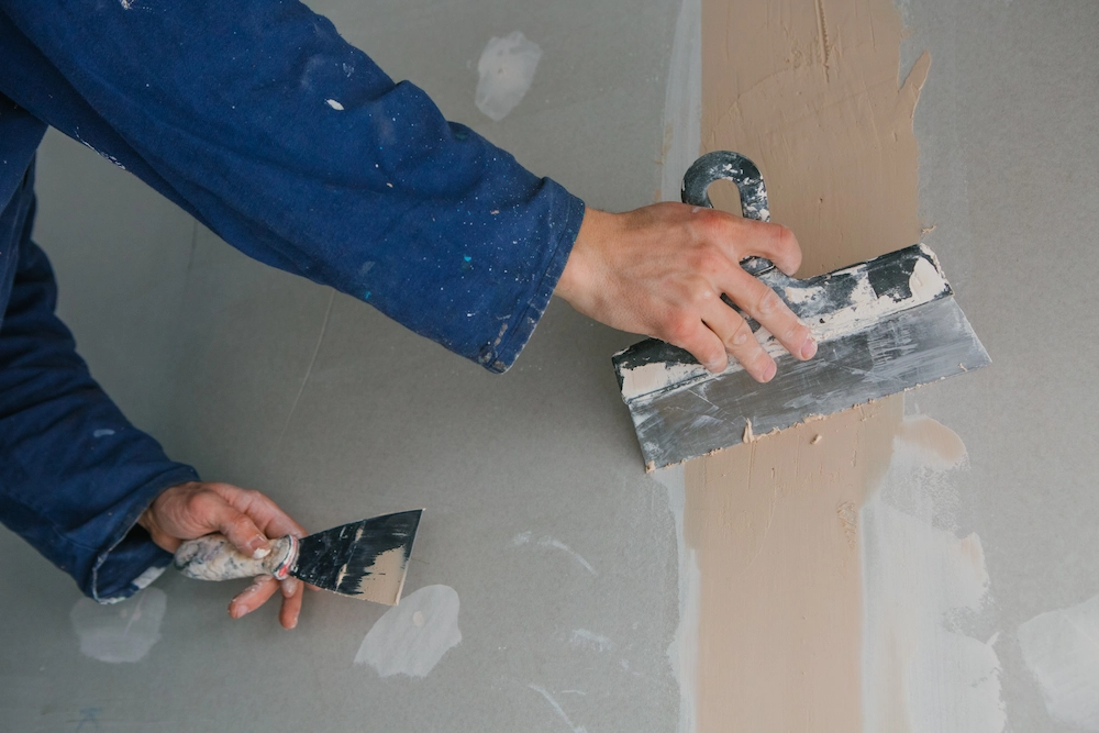 Worker applying wall putty to repair internal water damage