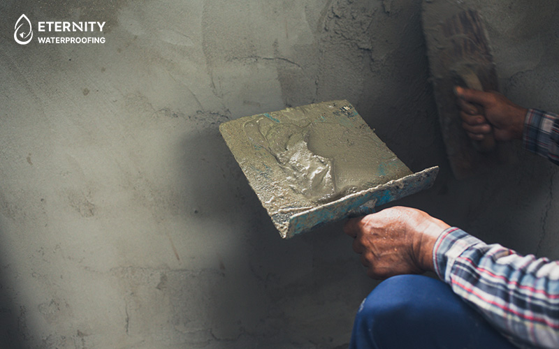Person in plaid shirt applying cement to a wall with a trowel.