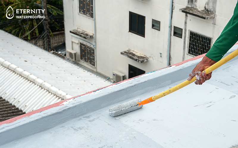 Person using a roller to apply waterproof coating on a flat roof.