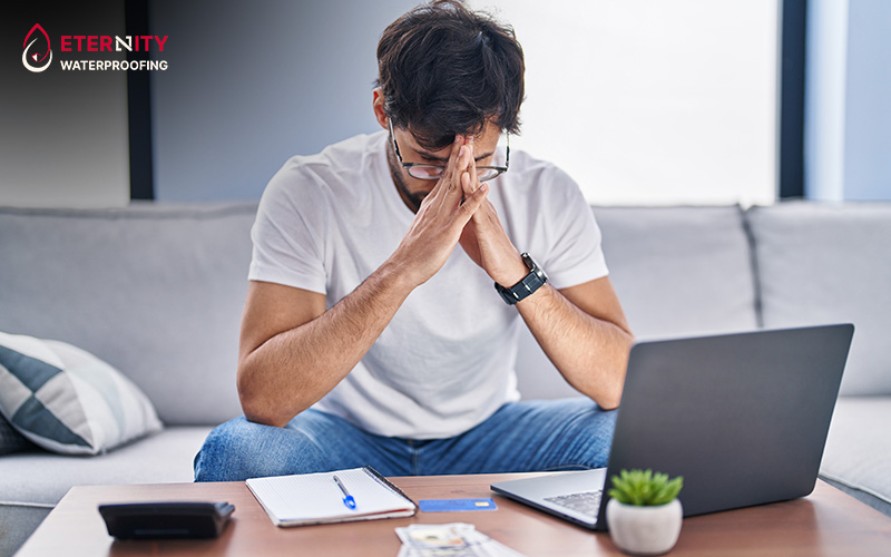A distressed man looking at a laptop, calculating repair costs